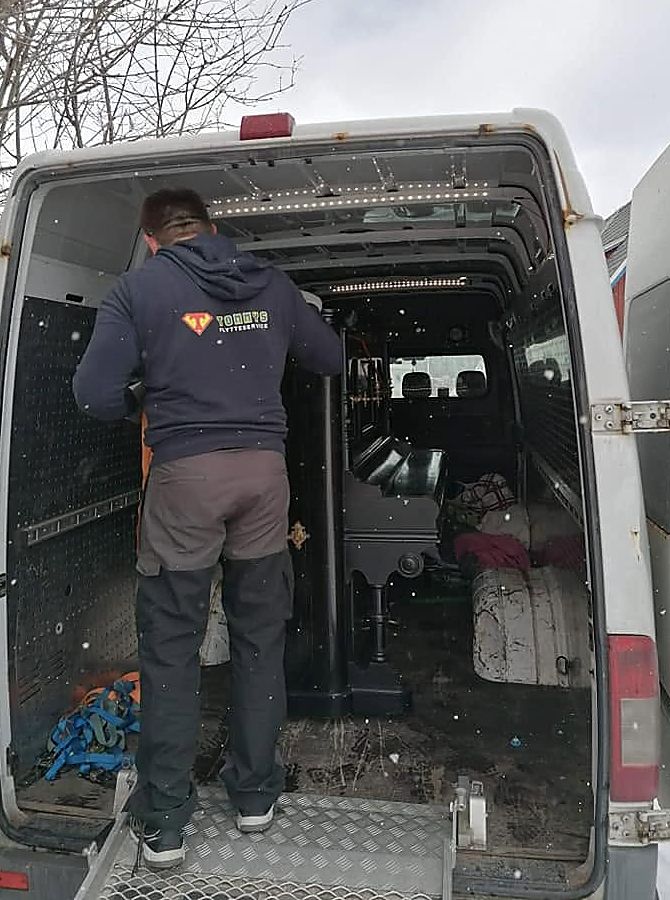 Ansatt i genser med firmalogo laster en flyttebil på vinterføre.